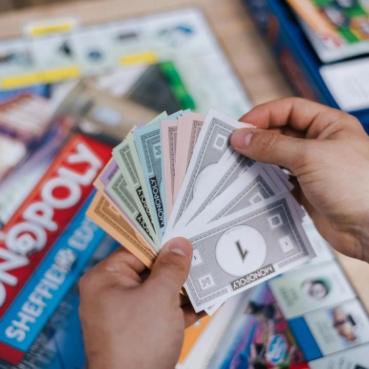 Spending money and budgeting when moving out – like in Monopoly! Person fanning out Monopoly fake money bills